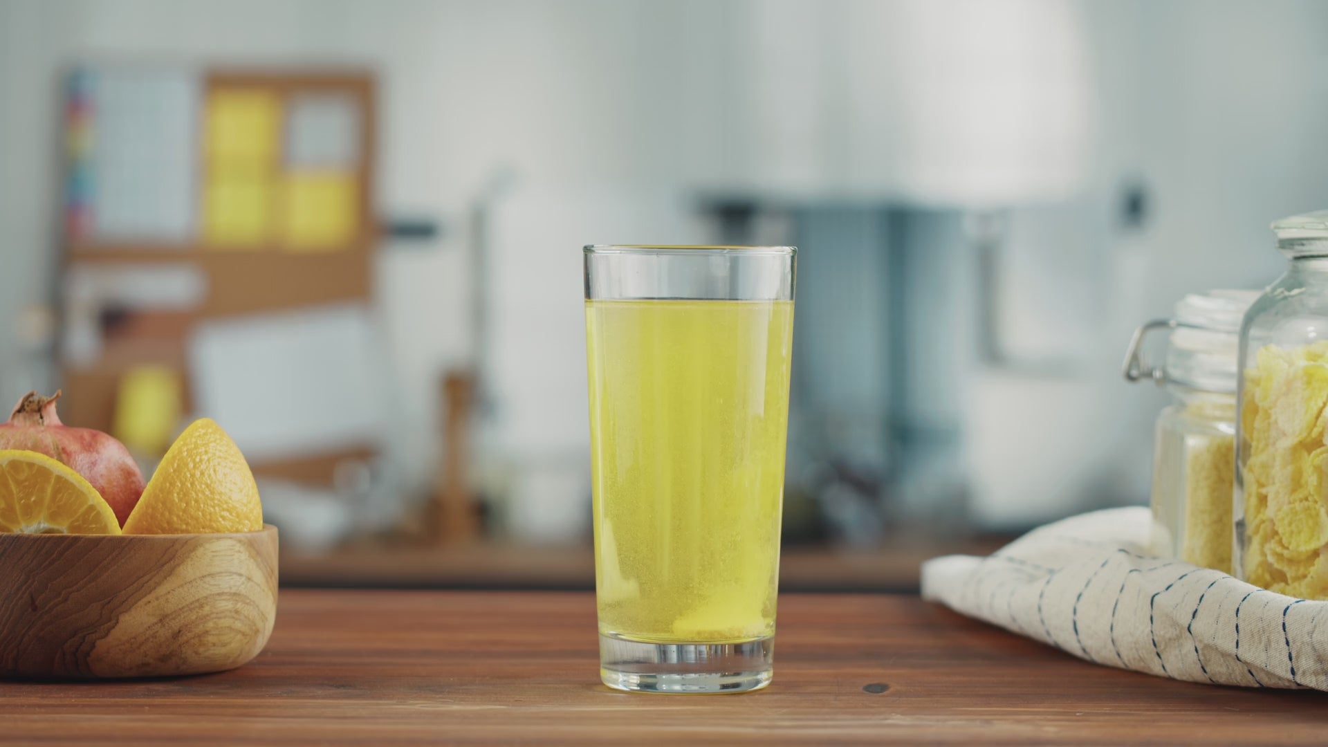 Load video: Orange KSP tablet dissolving in glass of water on a table.
